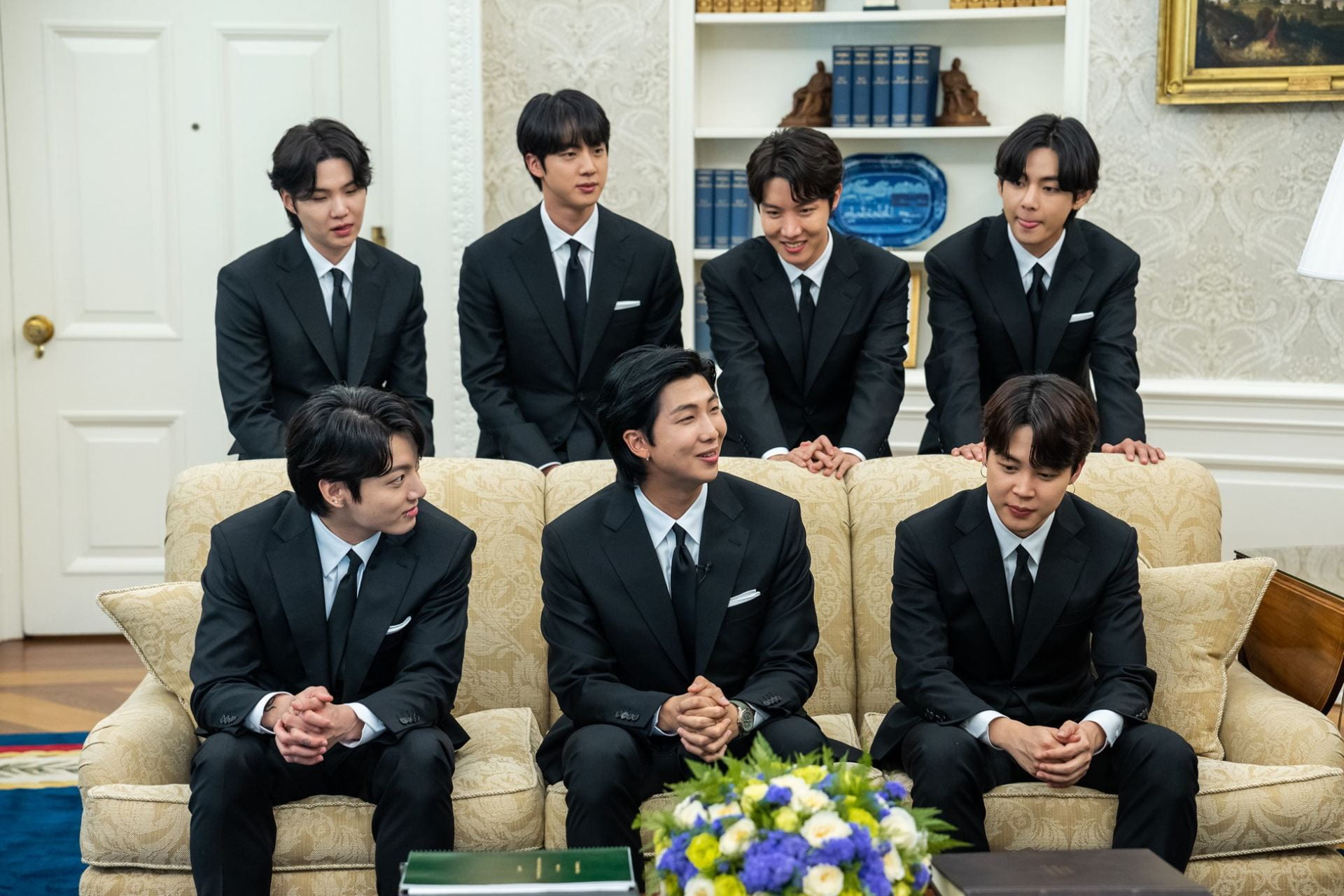 Members of BTS, dressed in suits, in the Oval Office.