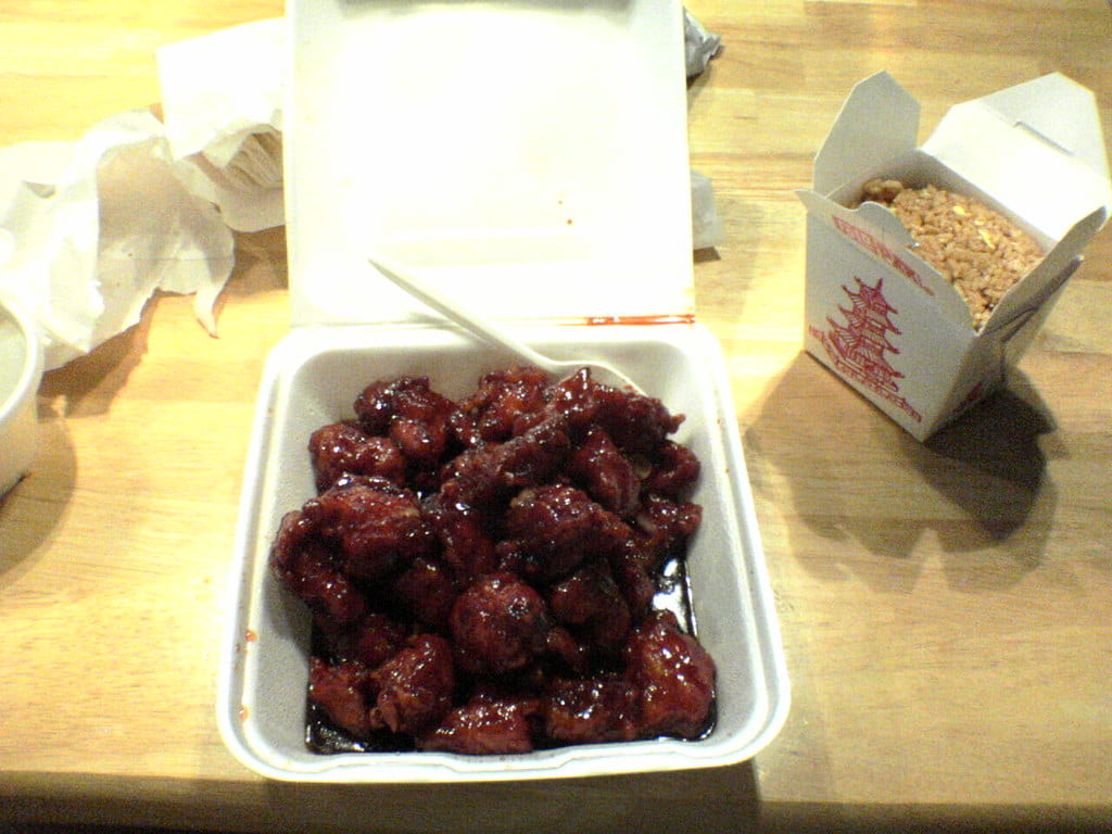 A takeout container with General Tso's Chicken with a side of rice.