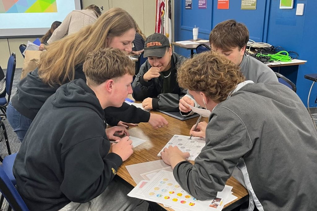 Students gathered at a table play a misinformation escape room game.